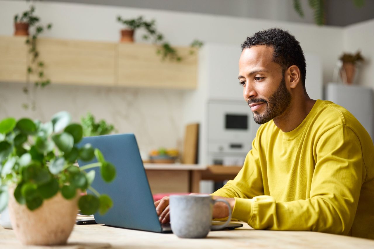 Man working on laptop at kitchen table with coffee mug