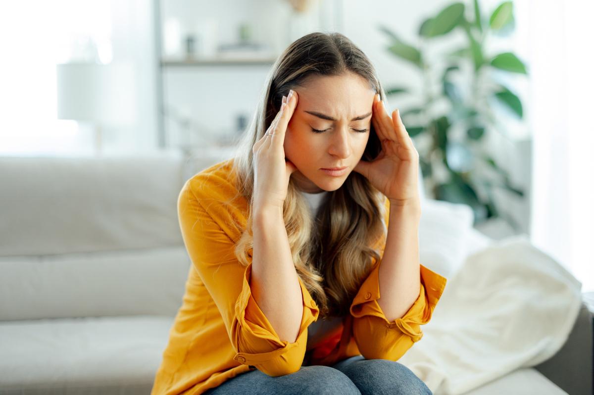 Woman holding her head with both hands, experiencing a headache at home