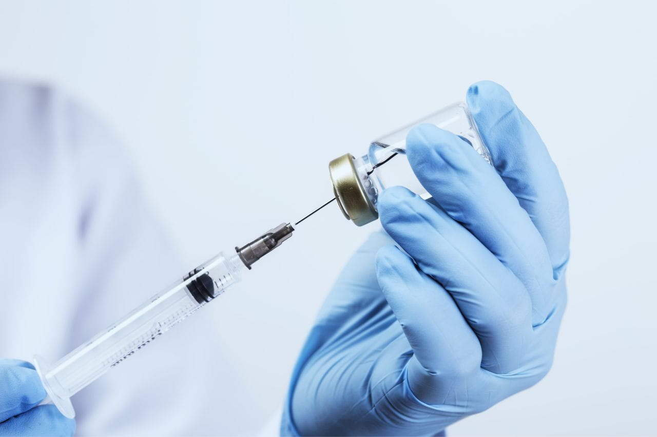 Gloved medical worker with a needle and vial of medicine