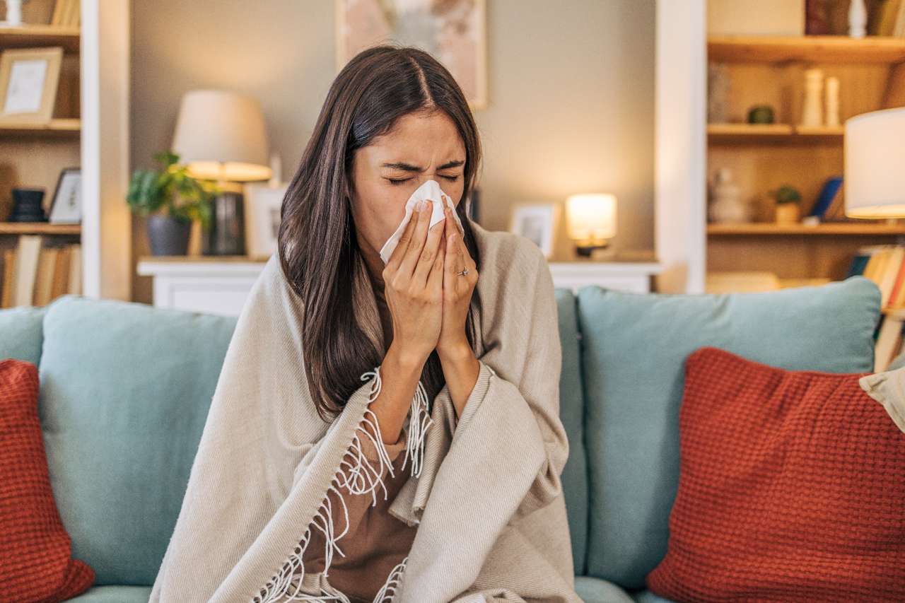 Woman sneezing into a tissue while sitting on the couch