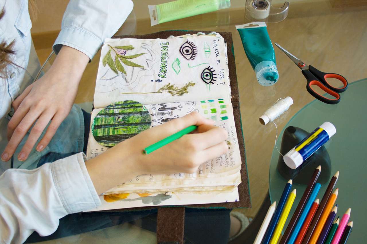 Person sketching in art journal with colorful supplies.