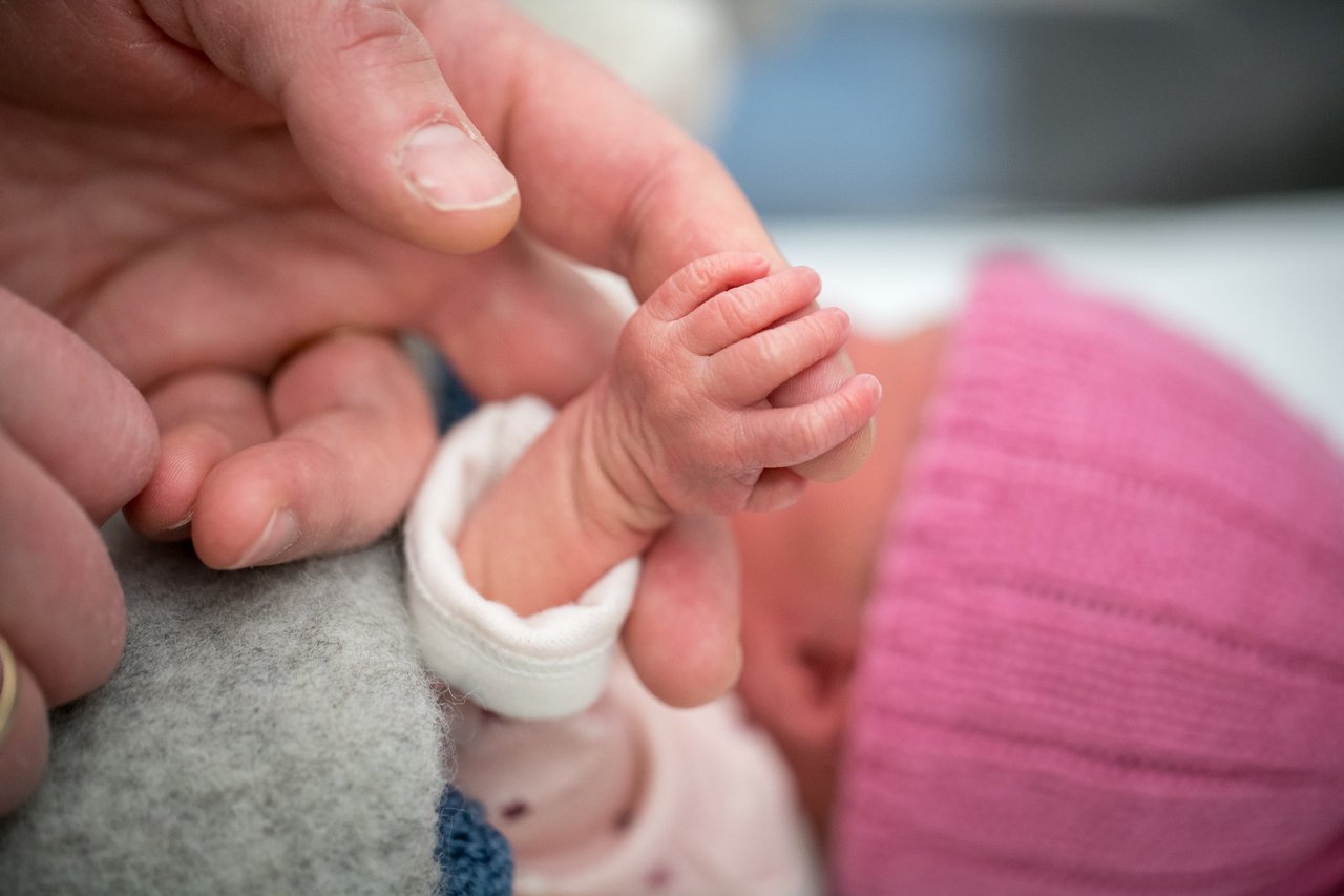 Preemie baby holding adult finger