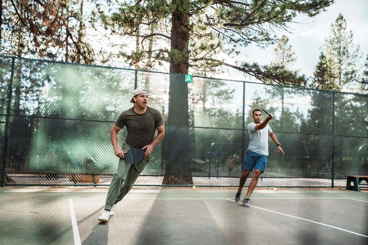 Two people moving quickly and leaning heavily to one side while playing pickleball outside