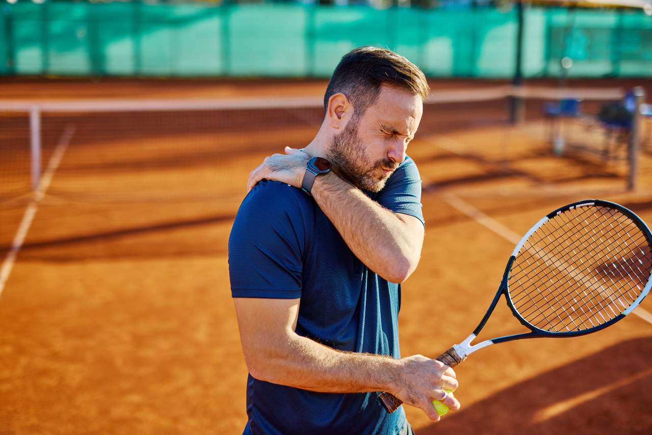 Tennis player holding his shoulder in pain while standing on a clay court.