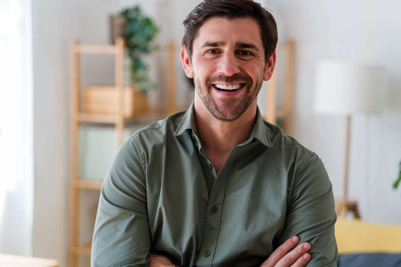 Smiling man standing indoors with arms crossed.