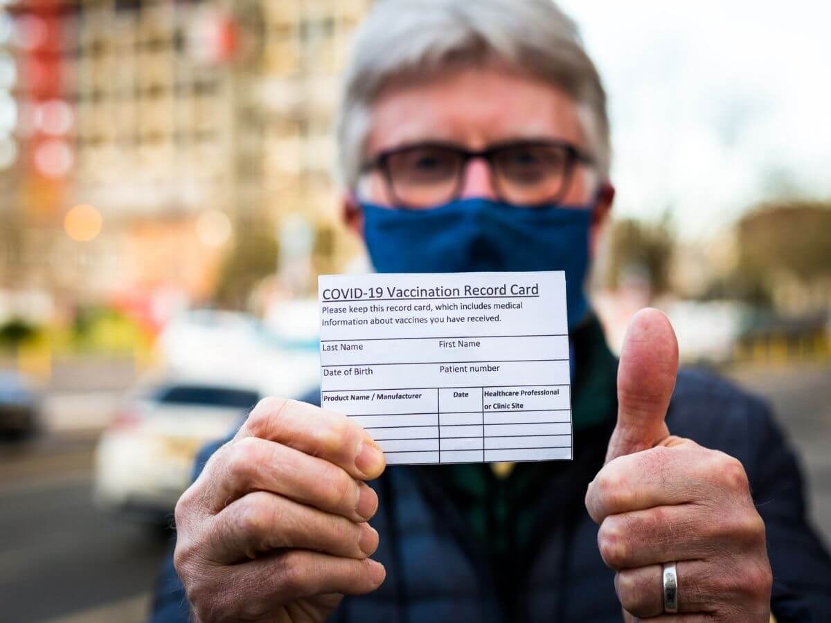 Man showing his COVID-19 vaccination card and giving a thumbs up