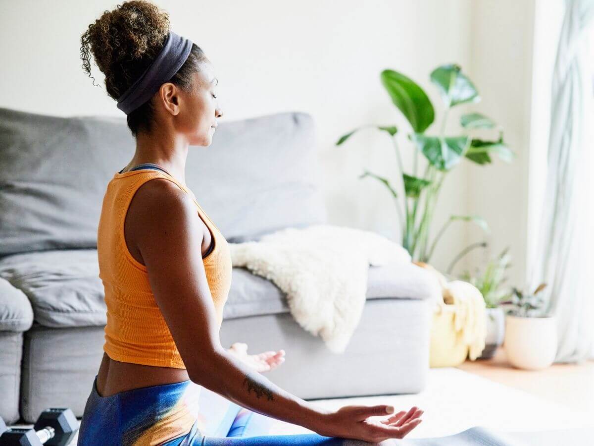 Woman sitting on the ground in her living room meditating