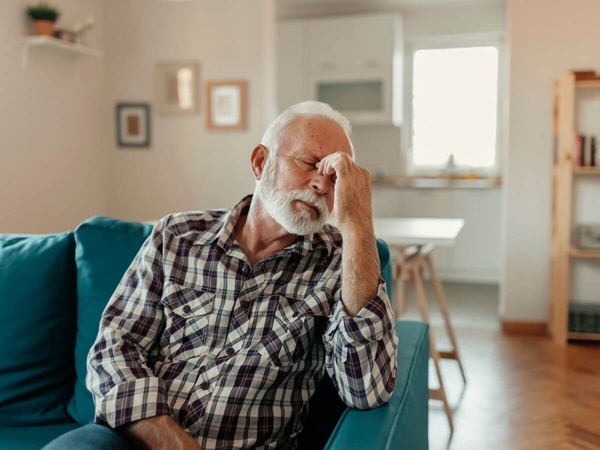 Older man sitting on the couch, looks to be in pain