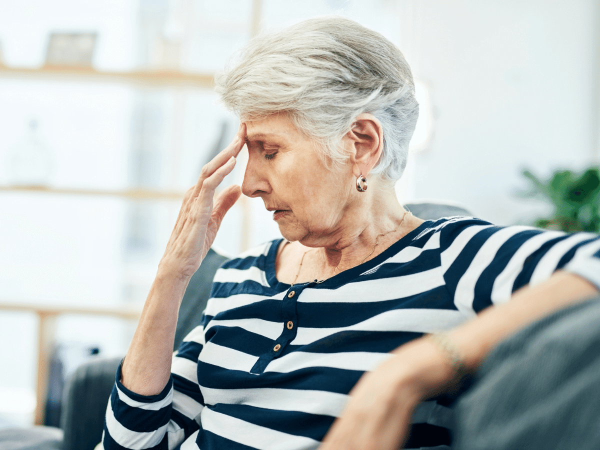 Elderly woman sitting on the couch holding her head in pain