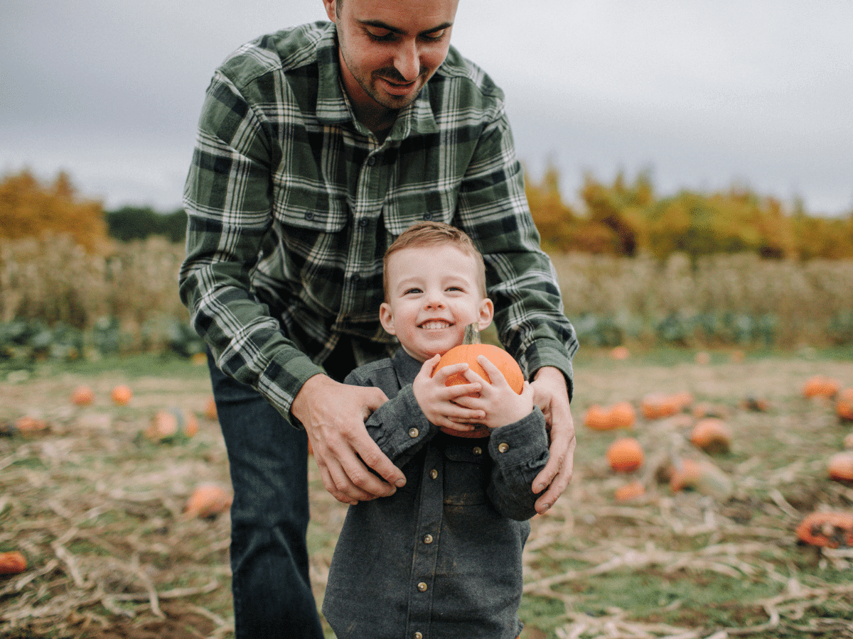 Father guiding young son through a pumpkin patch
