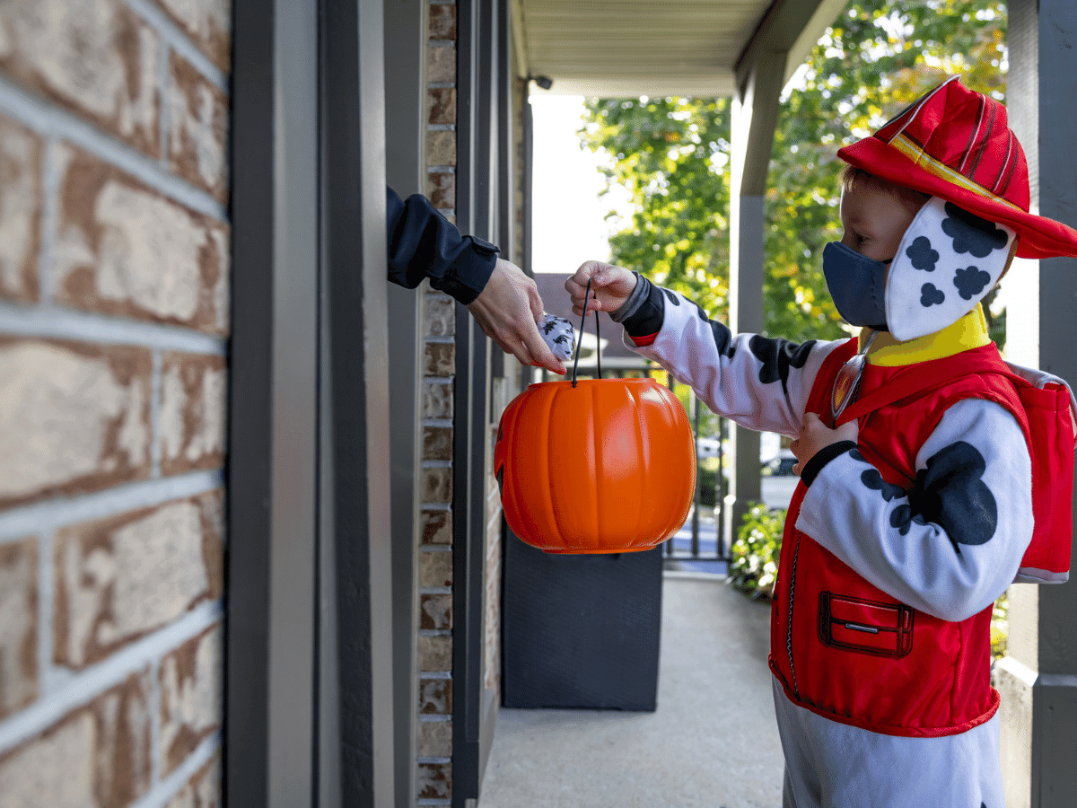 Young boy wearing a protective mask and costume trick or treating on Halloween.