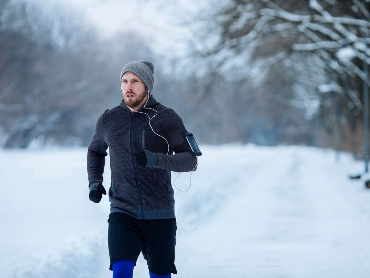 Man wearing winter clothing and hat running outside in the snow.