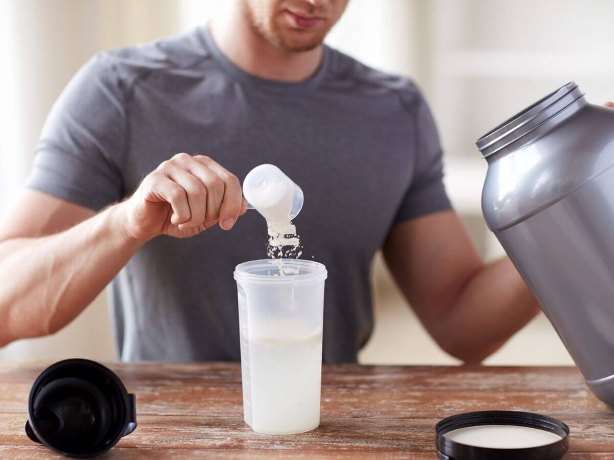 Man adding powdered nutrition supplement to a blender bottle