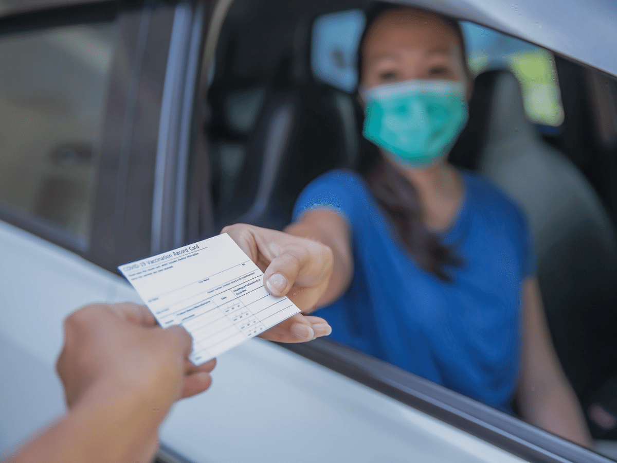 Woman wearing a mask showing her COVID-19 vaccine card to someone