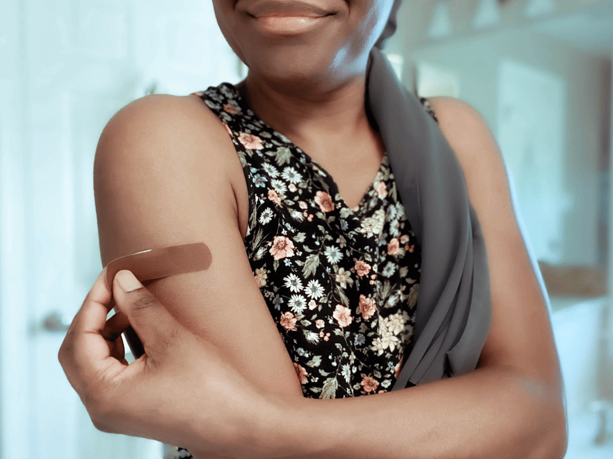 Young woman showing band-aid on upper arm from vaccination.