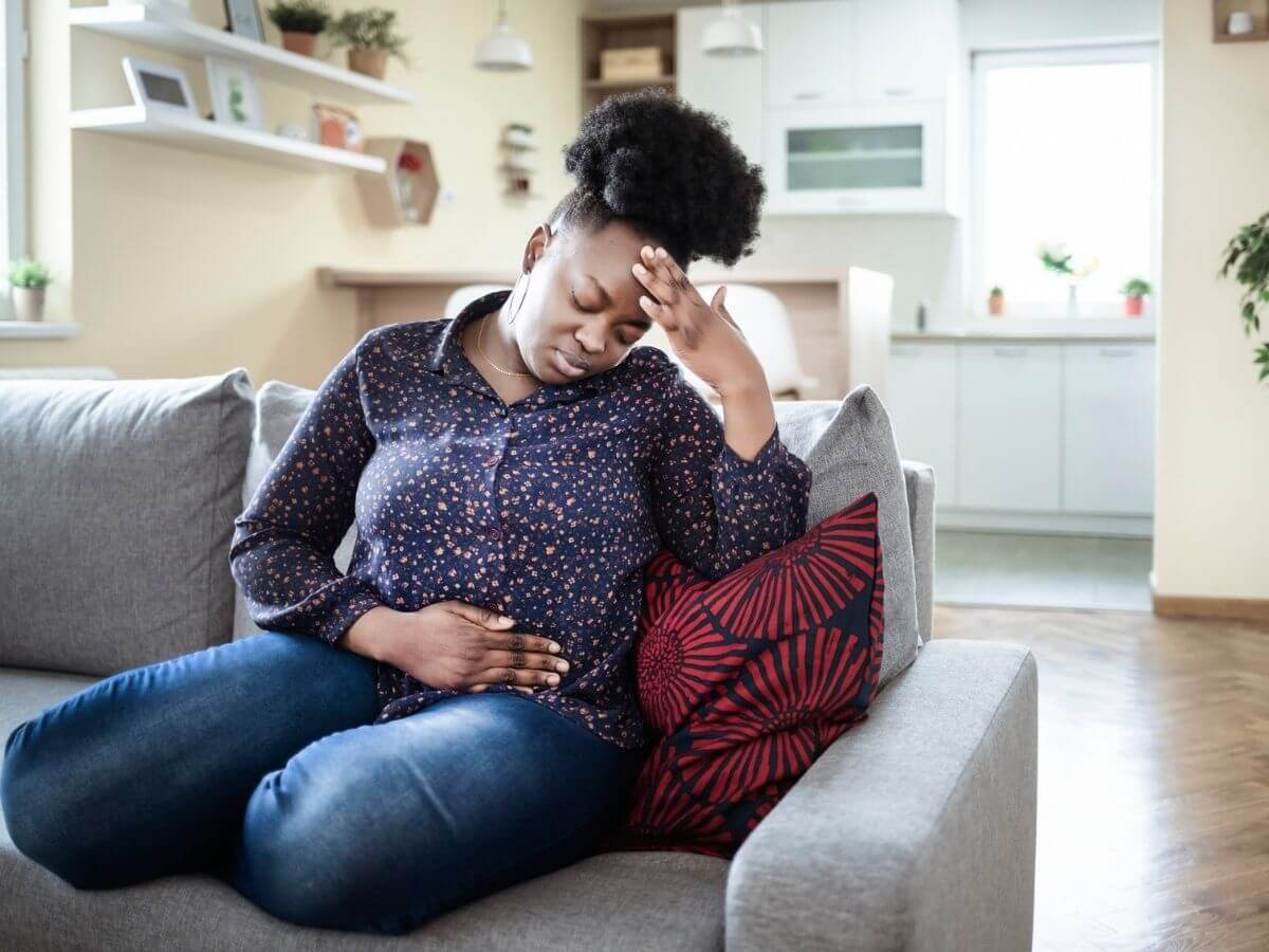 Woman sitting on a couch with one hand on her stomach and the other hand holding her head