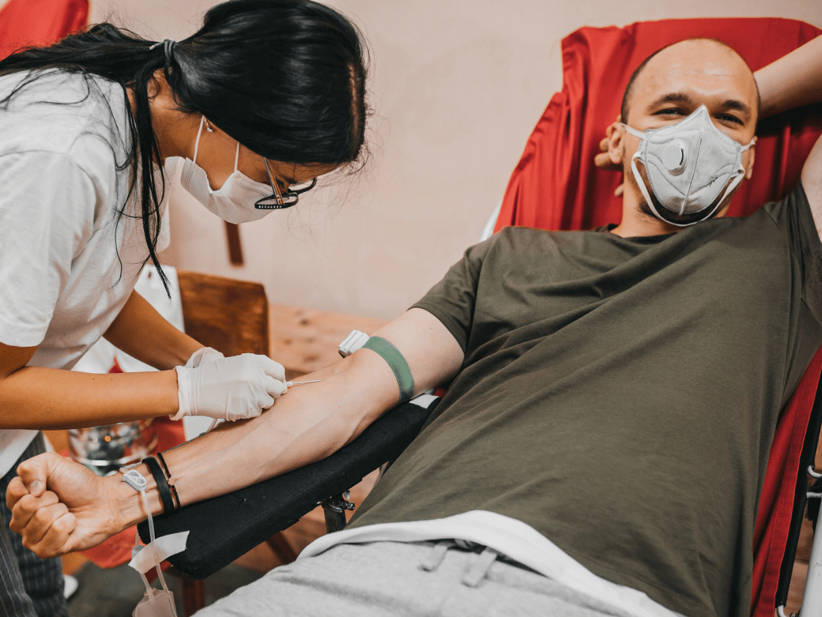 Man in protective mask reclines in a chair while donating blood
