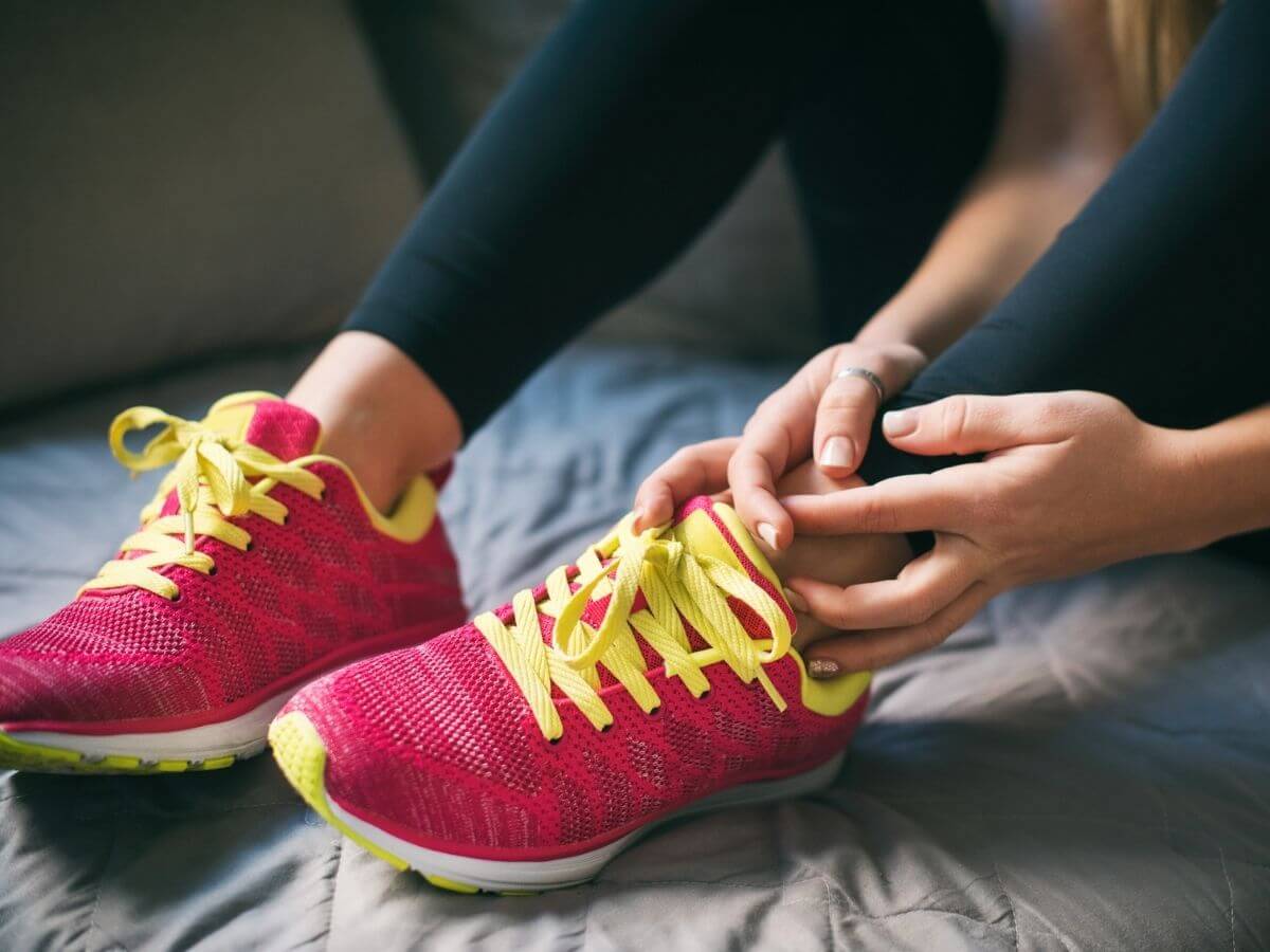 Close up of a woman lower leg and feet. She is wearing running shoes and holding one ankle with both hands.