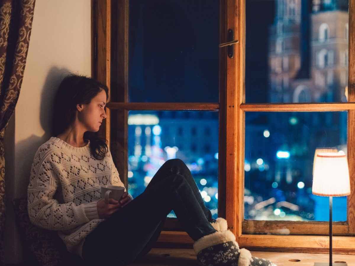 Sad young woman looks out a window during the holiday season