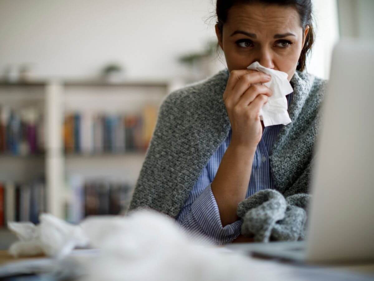 Woman blowing her nose while completing a virtual care visit on her computer