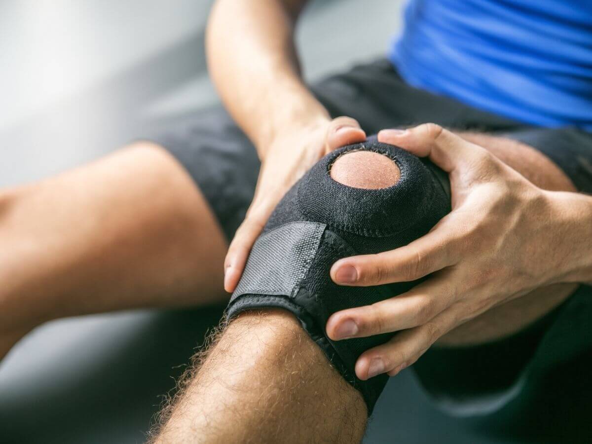 Close up of man wearing a knee brace, holding knee in pain