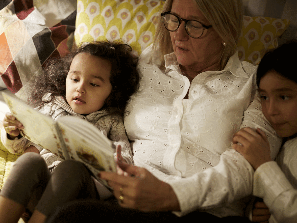 High angle view of grandmother reading book to granddaughters while lying on bed at home