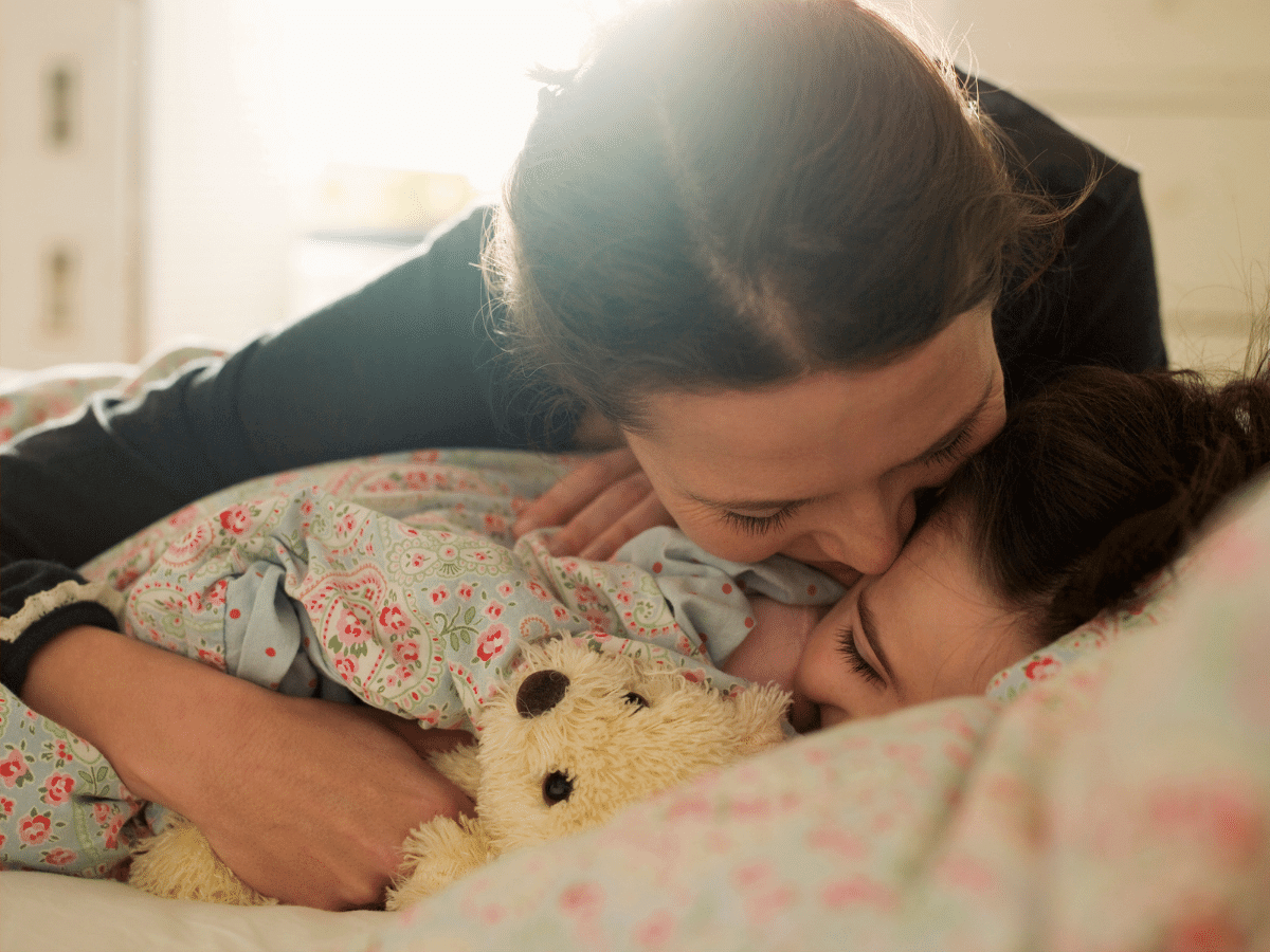 Mother wakes up young daughter in the morning with a kiss.