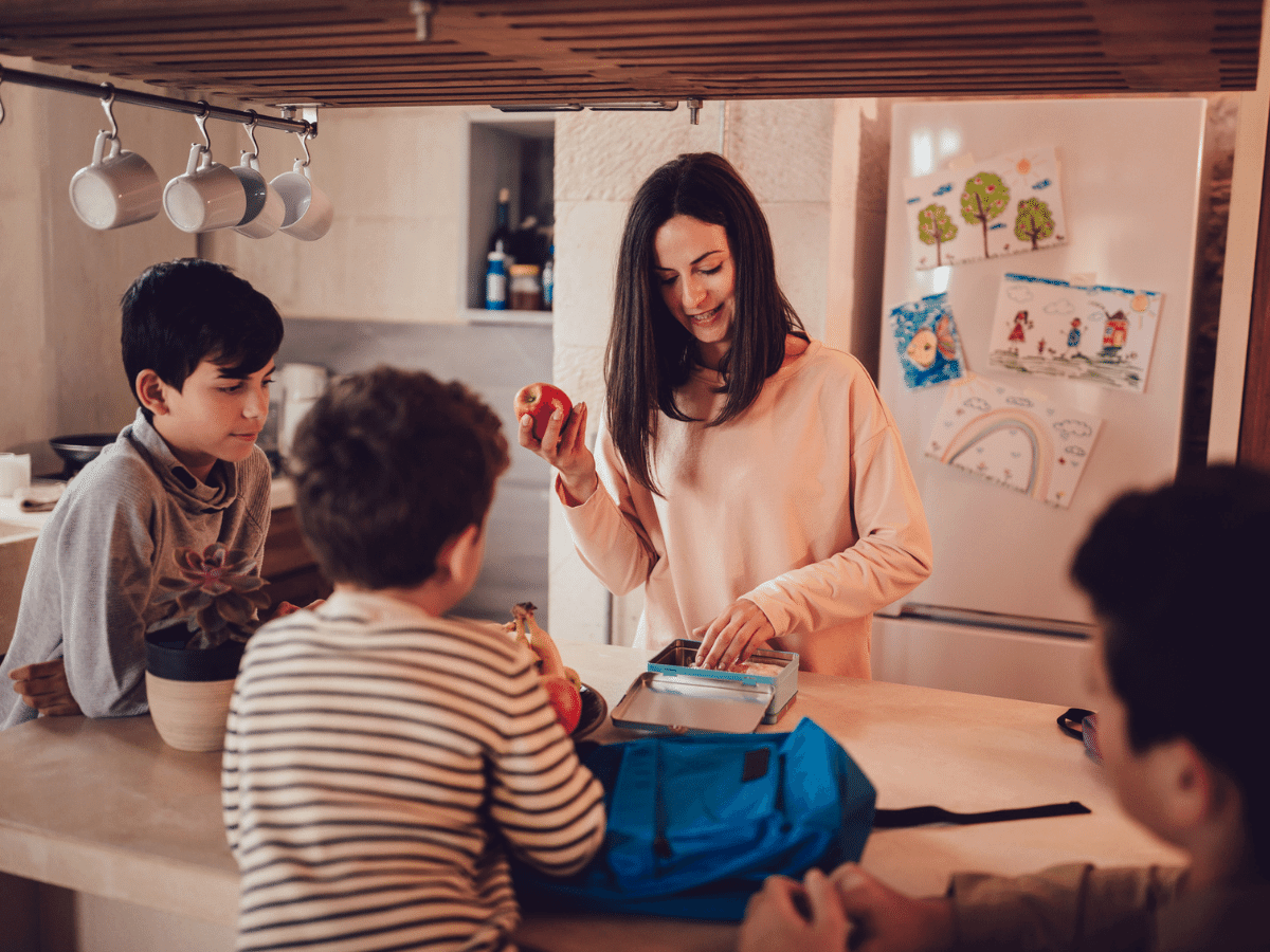 Mother preparing lunch boxes with healthy food and snacks for sons before going to school