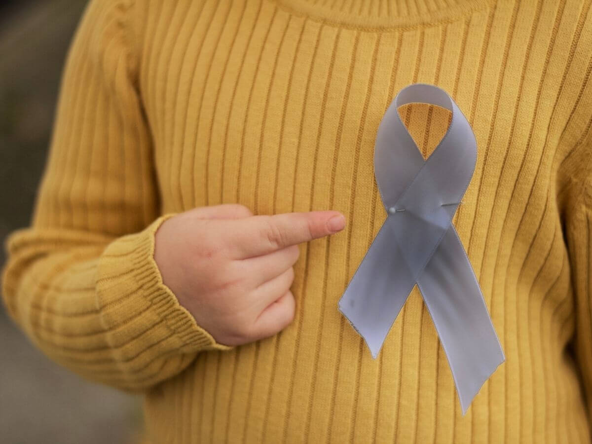Close up of a person's yellow shirt showing a silver awareness ribbon pinned to the chest