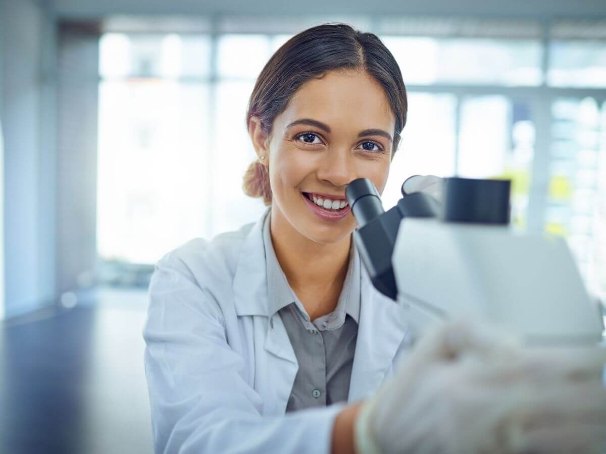 Female scientist smiling while using a microscope