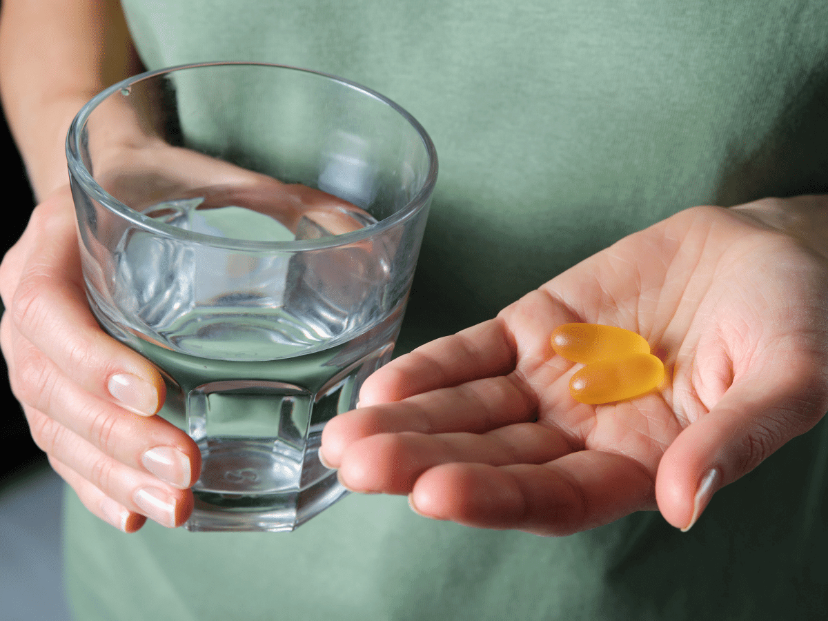 Close up of a woman holding omega-3 fish oil capsules and a glass of water.