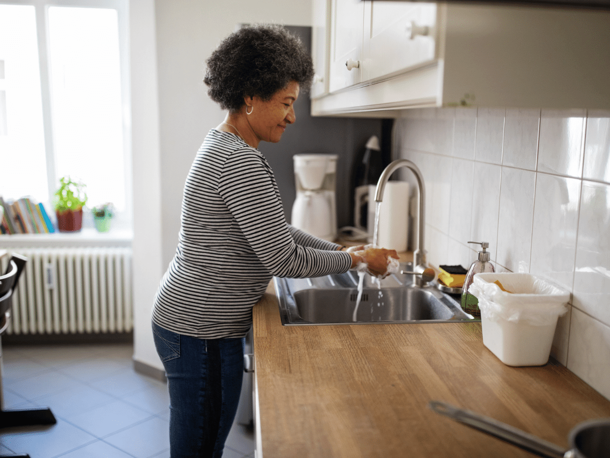 Middle-aged woman at home washing her hands in the kitchen sink