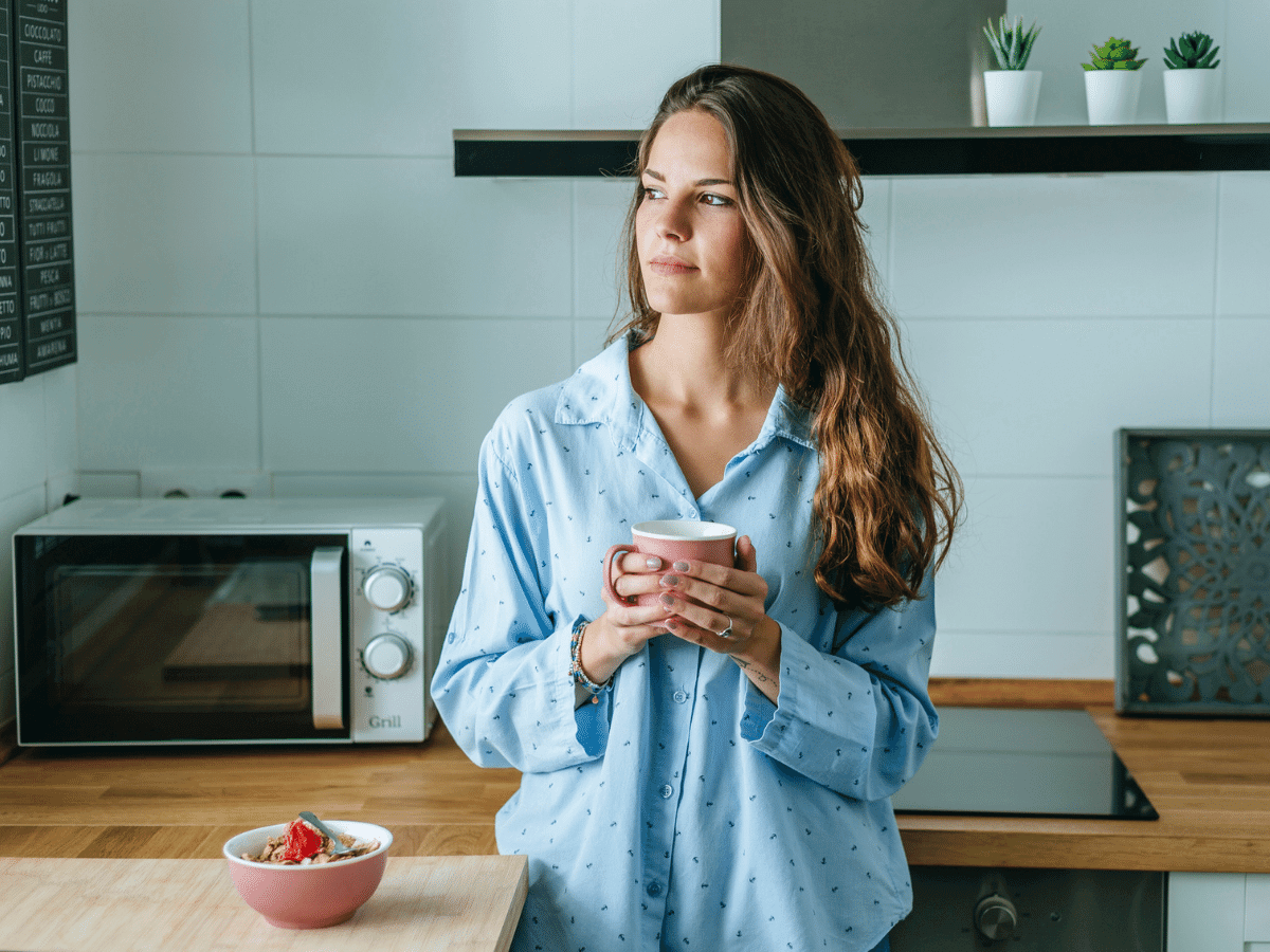 Woman holding a cup of coffee in the kitchen looking out the window.