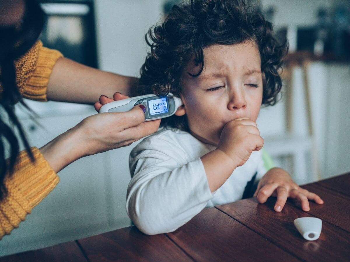 young boy coughing while mother takes his temperature