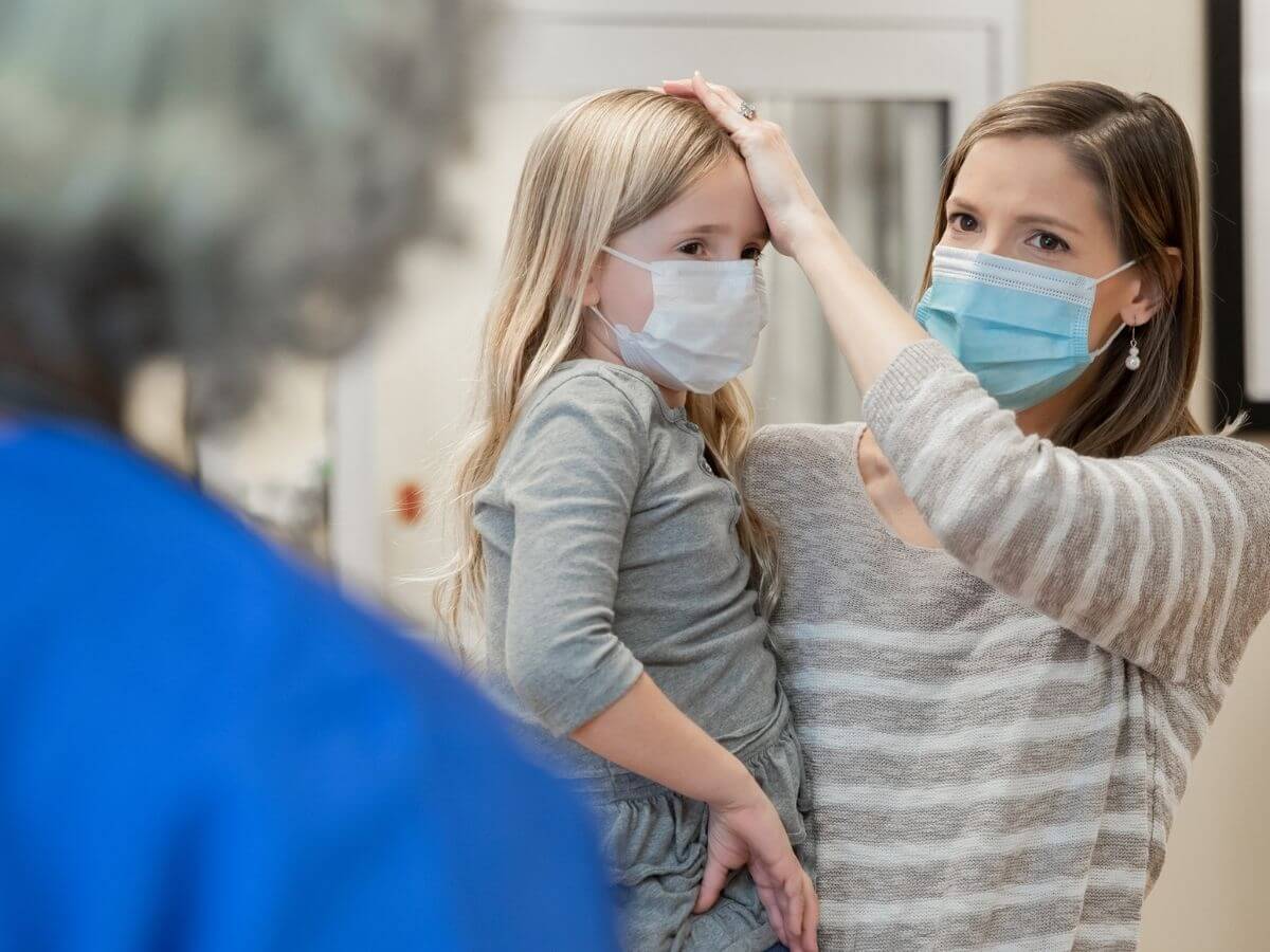 Mom holds daughter and feels her head for fever while talking to a nurse