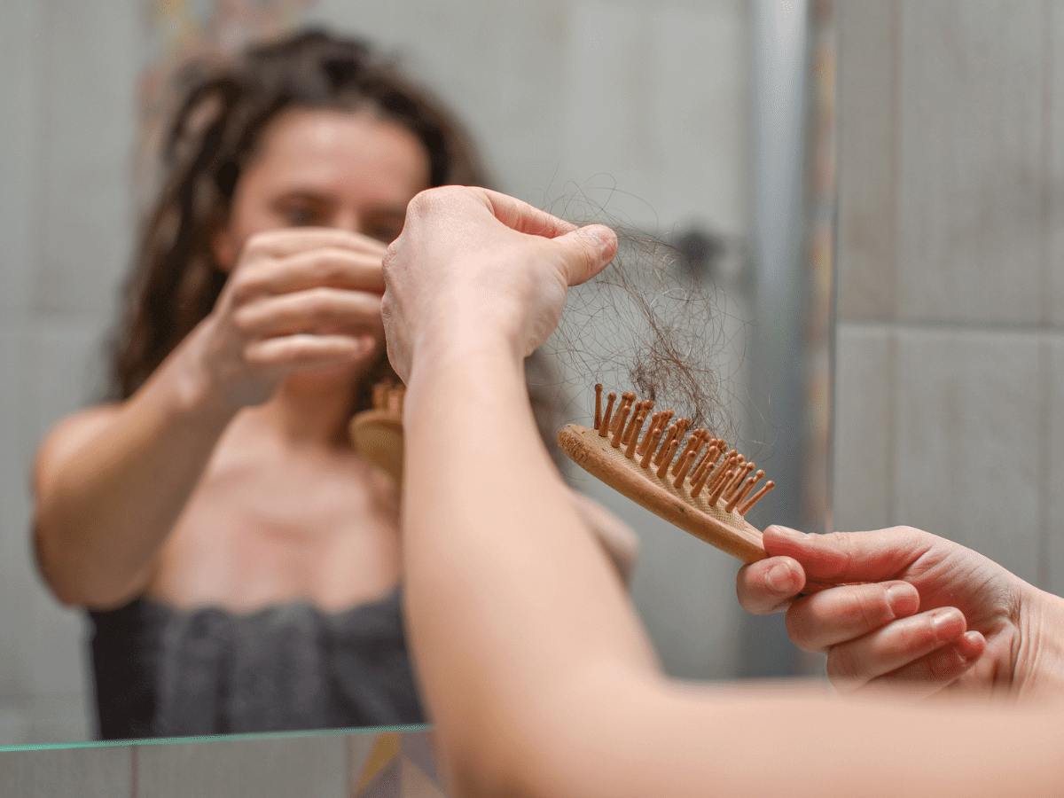Woman pulling hair out of a hairbrush in the bathroom