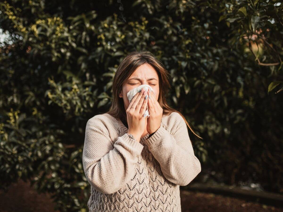 Woman in a sweater outside blowing her nose