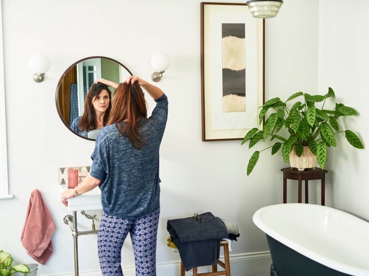 From back, woman looking at herself in a bathroom mirror