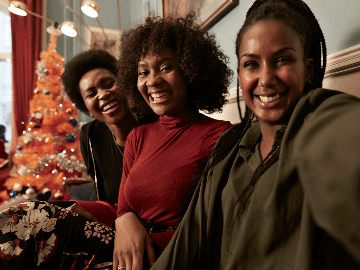 Three women laughing together on a couch in front of a Christmas tree