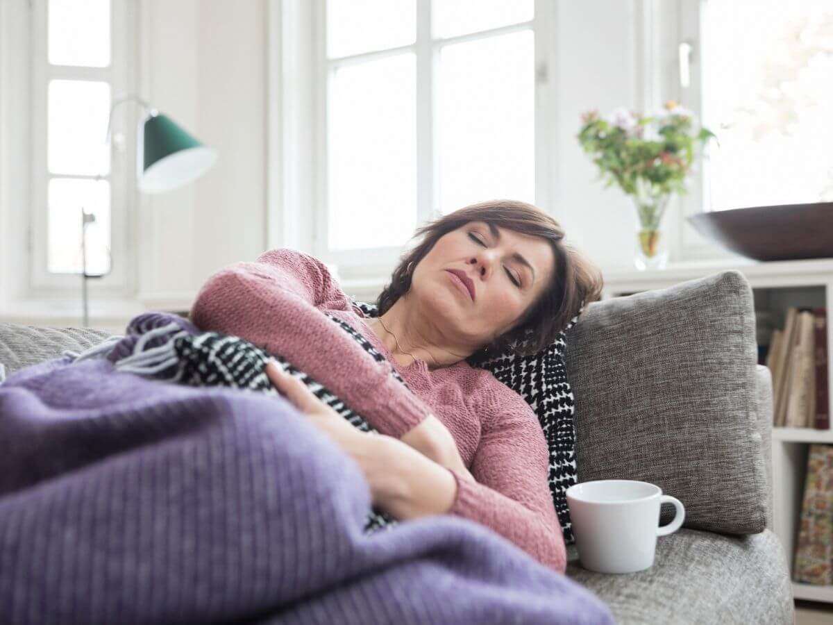 Woman laying on the couch holding her stomach in pain