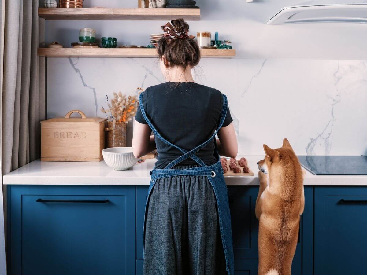 Photo of a woman and her dog standing at the counter in her kitchen cooking