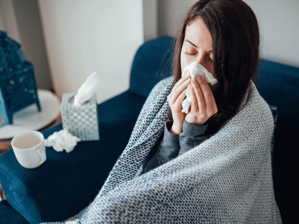 Woman covered in a blanket on the couch, blowing her nose