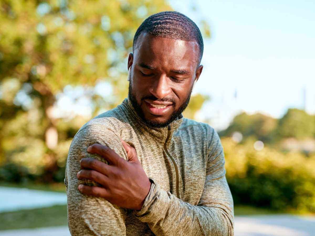 Man outside grabbing his shoulder in pain.