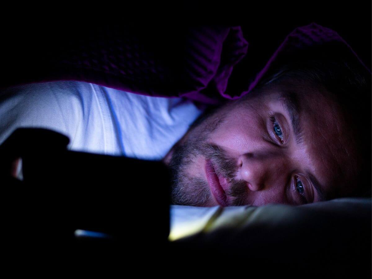 Close up of a man in bed at night, awake and looking at his phone