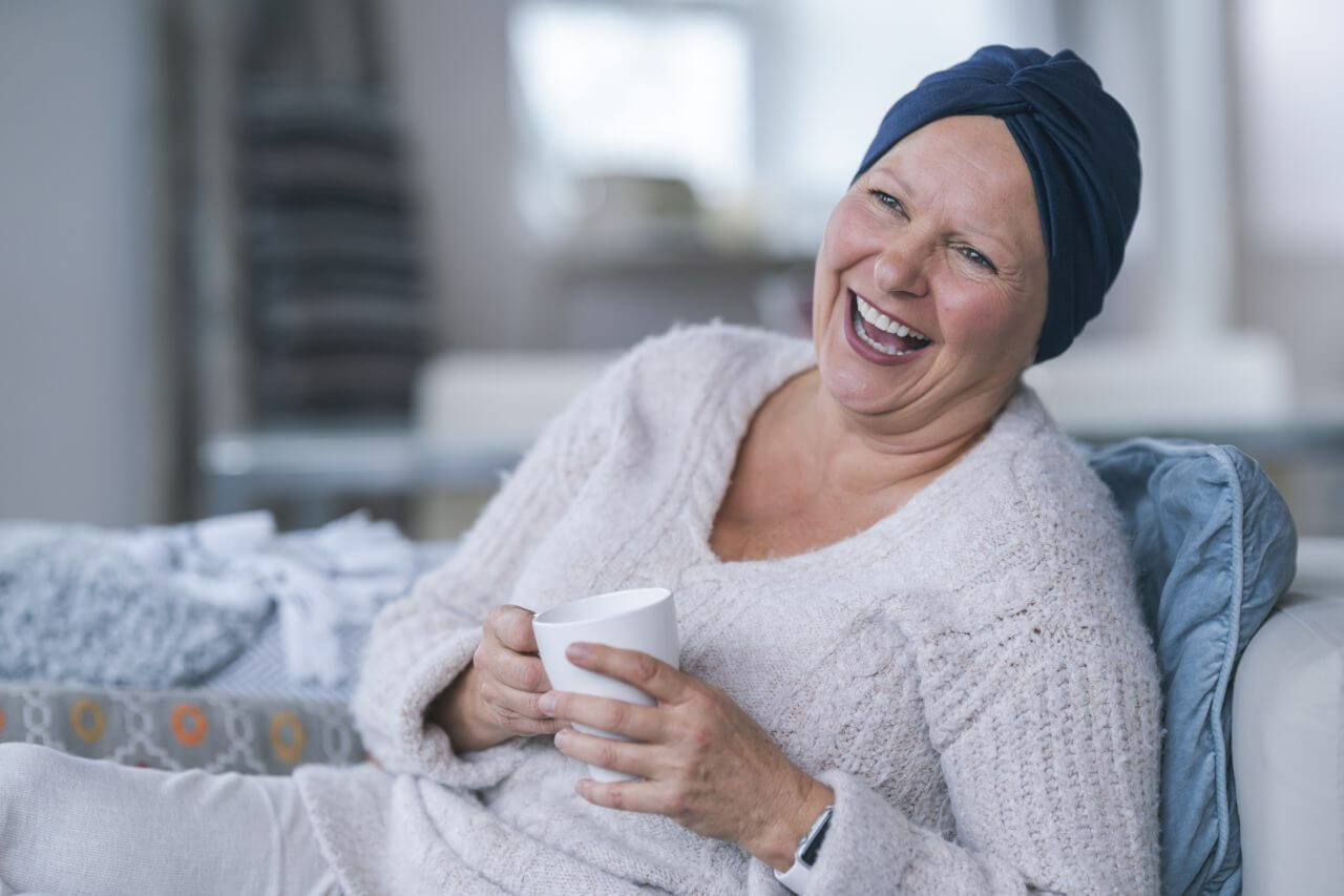 Woman who has lost her hair due to cancer treatment is smiling while holding a mug of coffee.