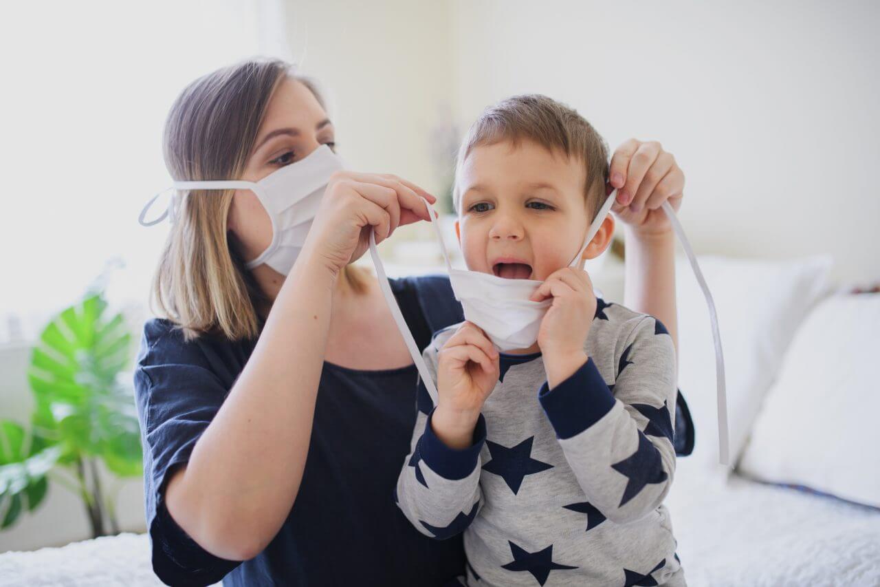 Mother wearing a disposable mask helps her young son put his face mask on