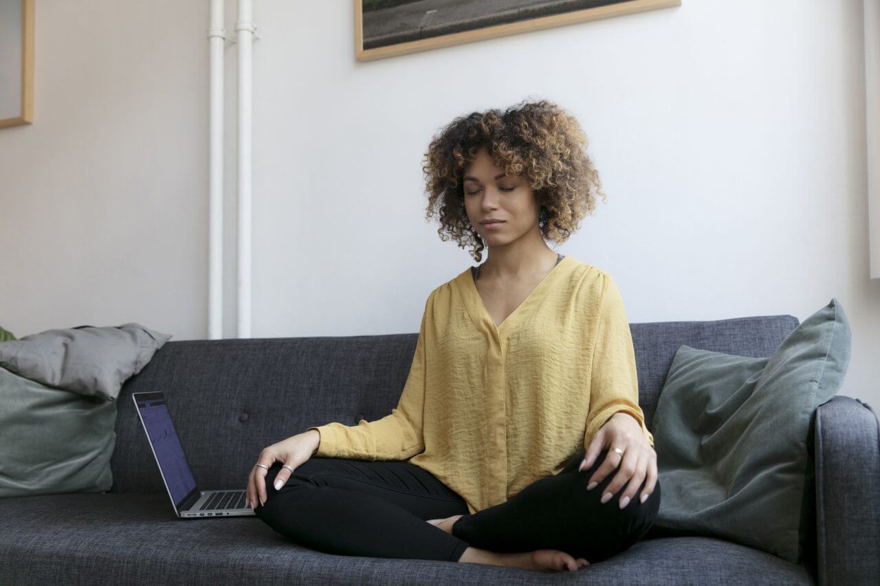 Woman sitting on the couch next to her laptop meditating