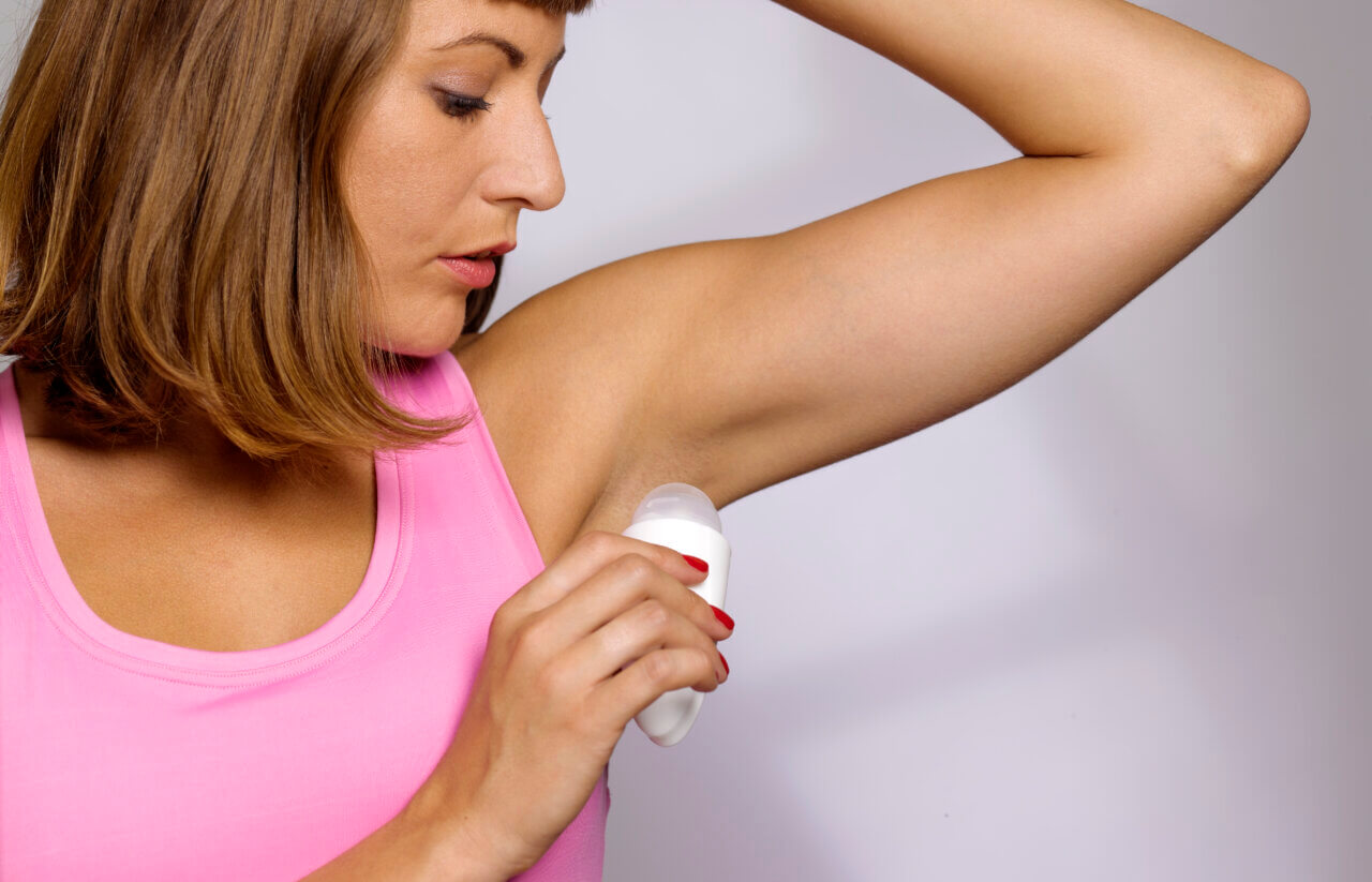 woman putting on deodorant to cover body odor