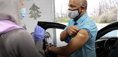 Man sitting in a car at a drive-through vaccination site pulling up his sleeve for a shot